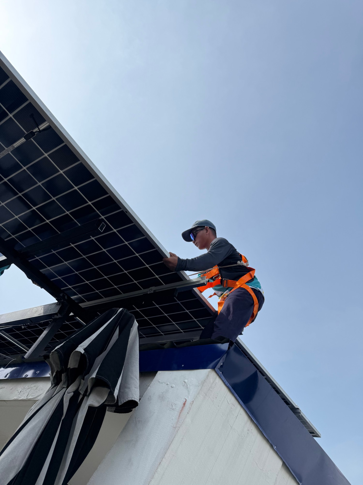 Installer mounting a solar panel on a rooftop edge against a clear sky