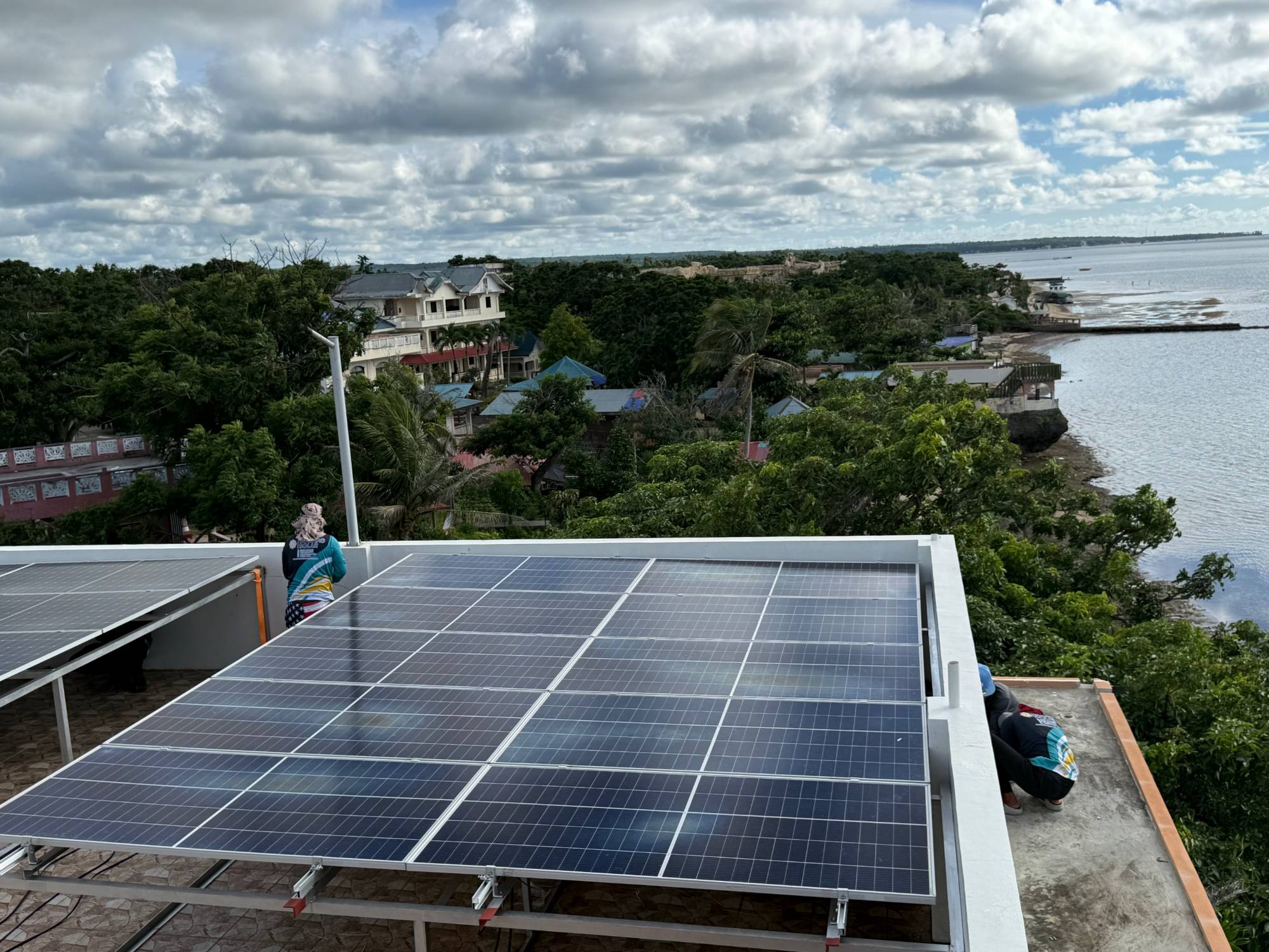 Rooftop solar array overlooking the coast, panels being fitted by an installer