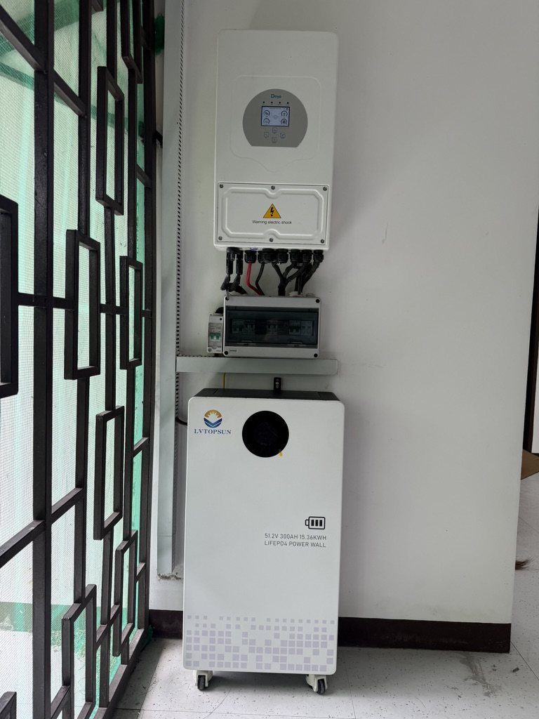 Hybrid solar inverter with its breaker box above a LiFePO4 battery, installed beside a window grille